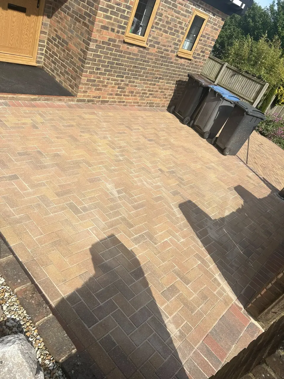 Block paving patio in the sun after cleaning, with bins and planters to the side