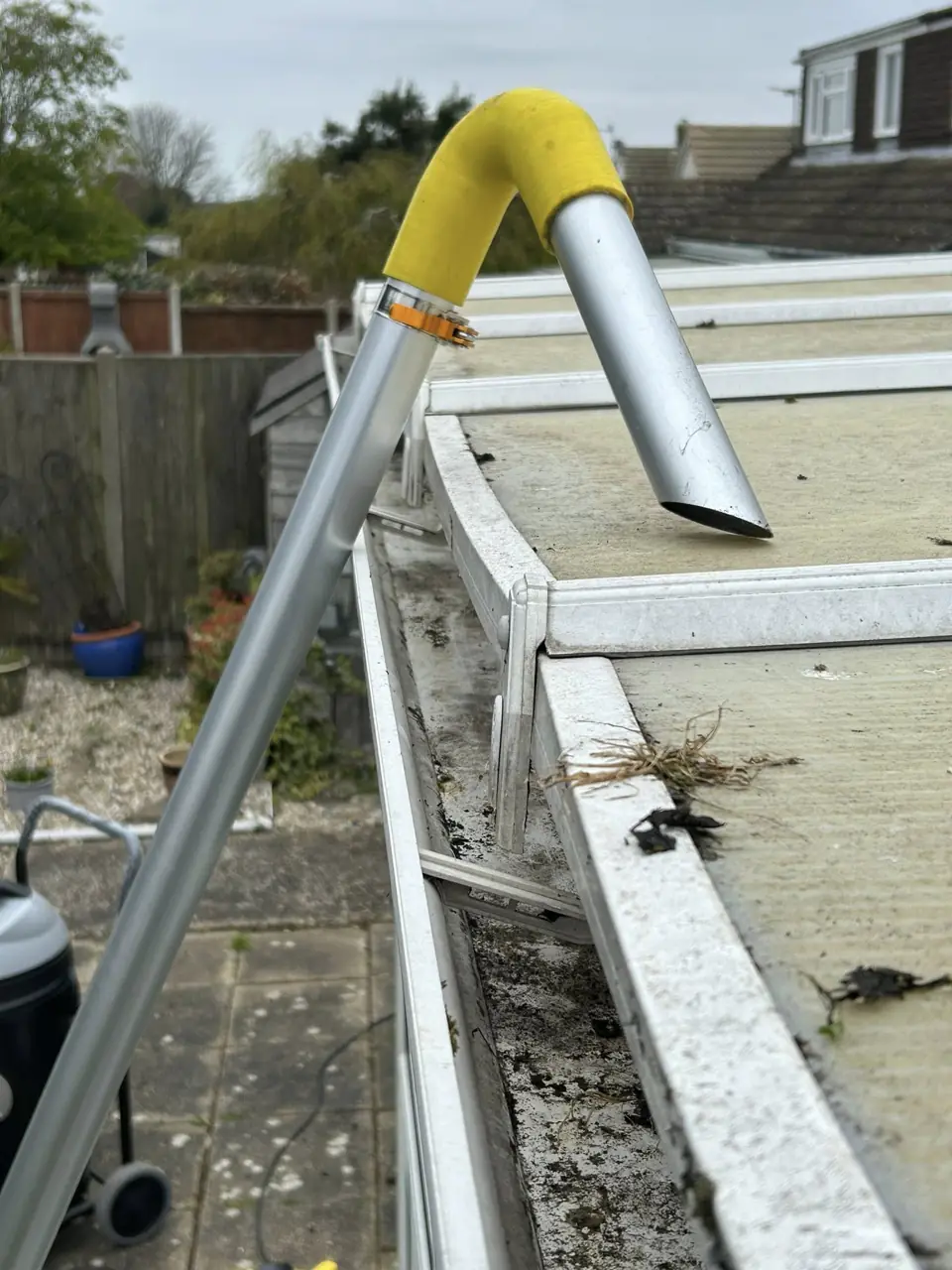 Gutter vacuum pole raised to a roof line to clear the gutter from the ground