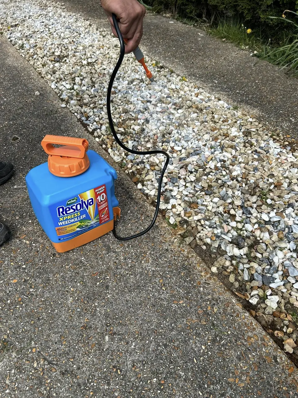 Weed treatment being sprayed along a gravel path beside a lawn